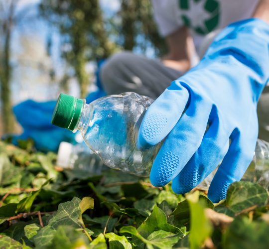 Man collecting plastic garbage in container in a polluted park. Rubber gloves, recycling signs on T-shirt